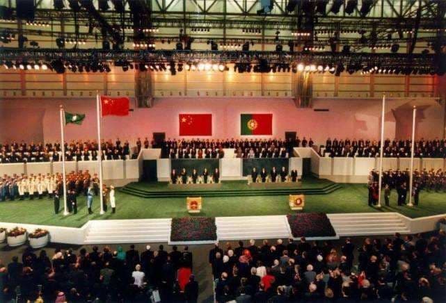 The sovereignty transfer ceremony at the Macau Cultural Centre, 20 December 1999. The national flags of the People's Republic of China and Portugal are displayed on the central stage as Chinese and Portuguese delegations mark the formal transfer of Macau to PRC sovereignty after more than 440 years of Portuguese administration. The flag of the newly established Macau Special Administrative Region is raised at left.